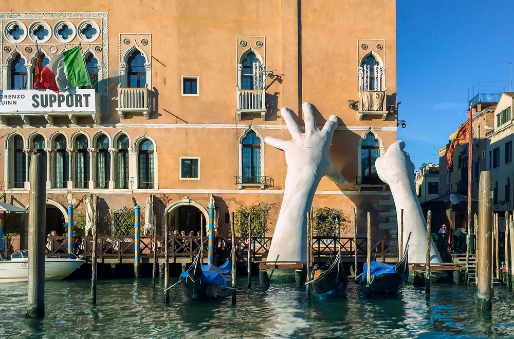 Socha rúk podopierajúca budovu na Grand Canal v Benátkach. Povodne pravidelne sužujú najromantickejšie mesto sveta a drasticky ničia vzácne pamiatky Zdroj: https://unsplash.com/photos/8v8TJkKX41Y. Foto: Sterling Lanier, 2020